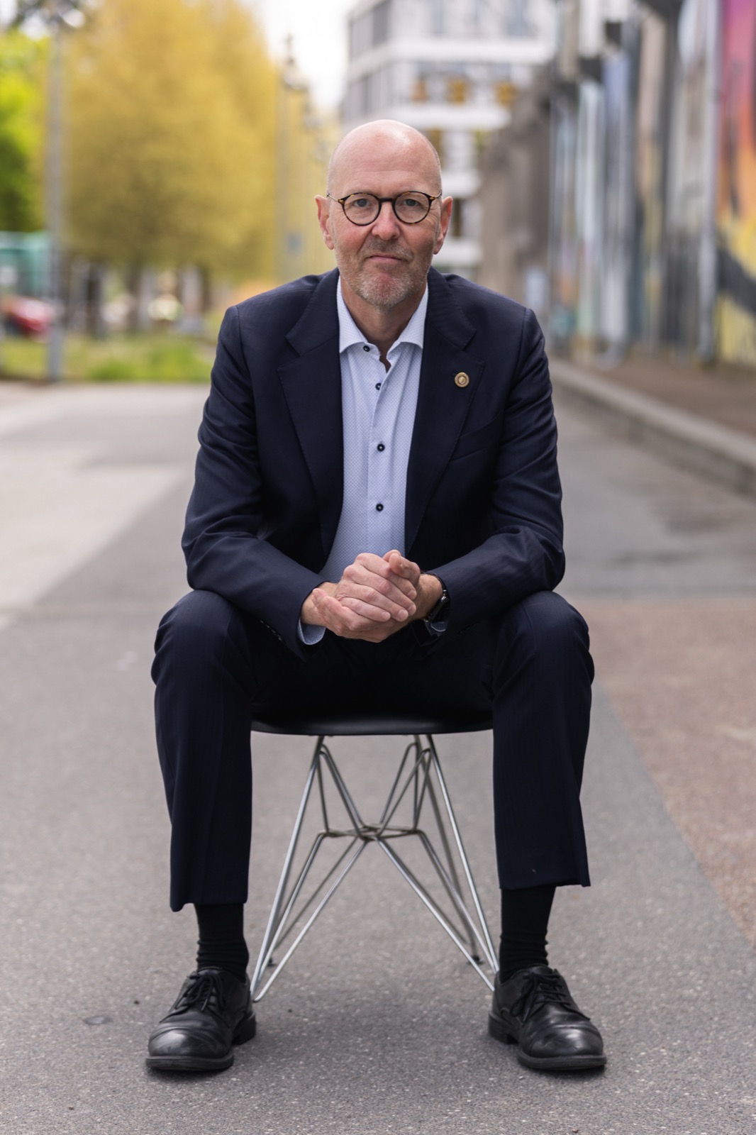 Per Beining seated on a chair in a Copenhagen street, hands folded, ready to listen