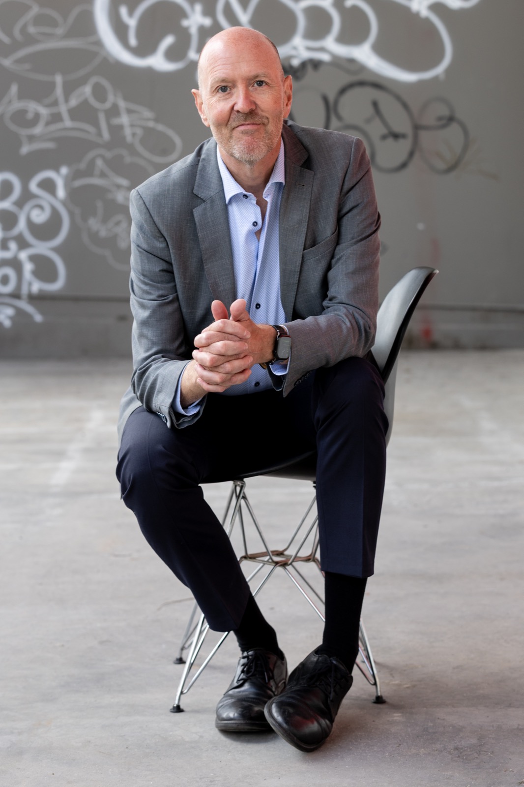 Per Beining sitting forward on a chair in front of a graffiti wall, hands folded — ready to talk