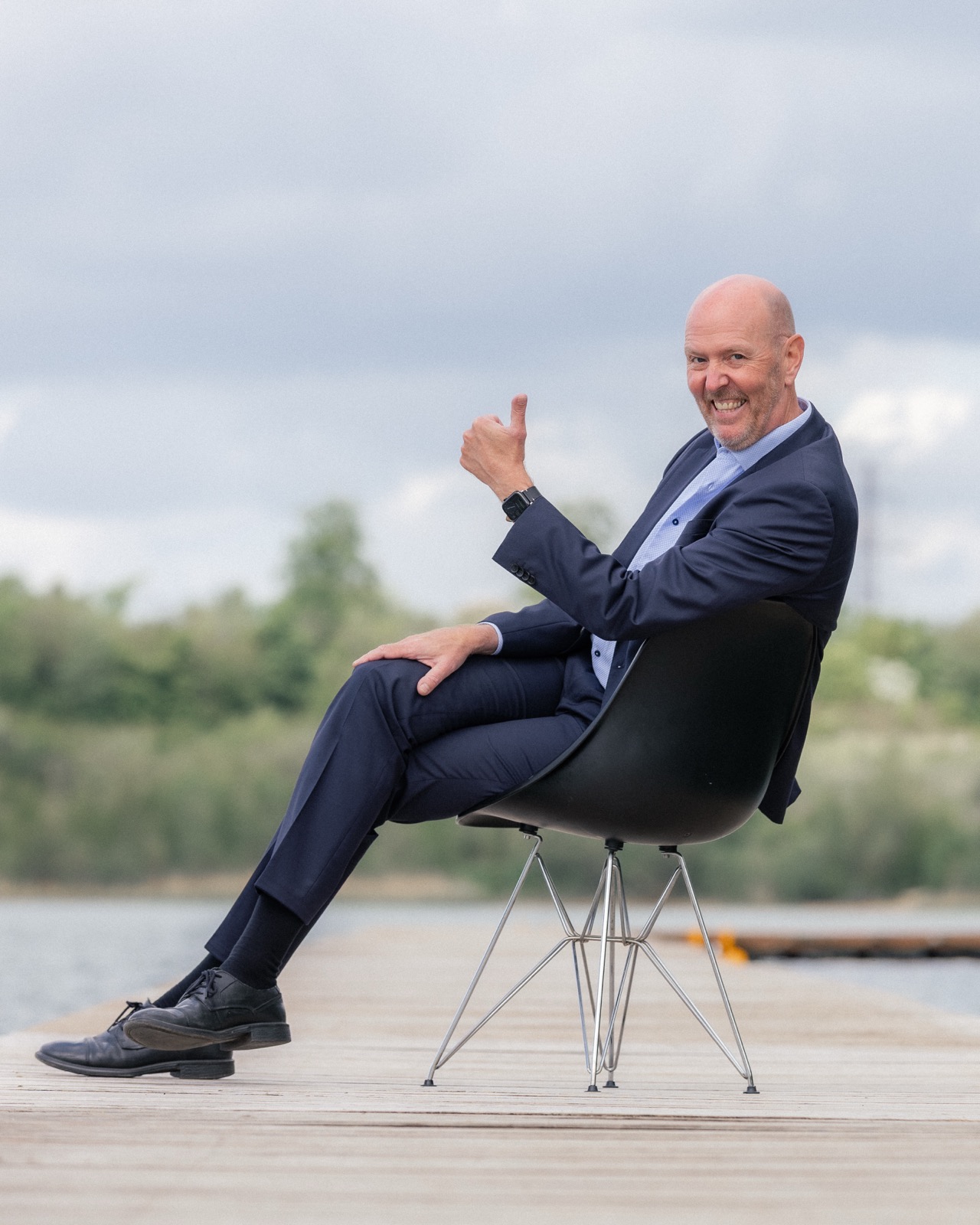 Per Beining laughing and giving a thumbs-up from a chair on a lakeside jetty